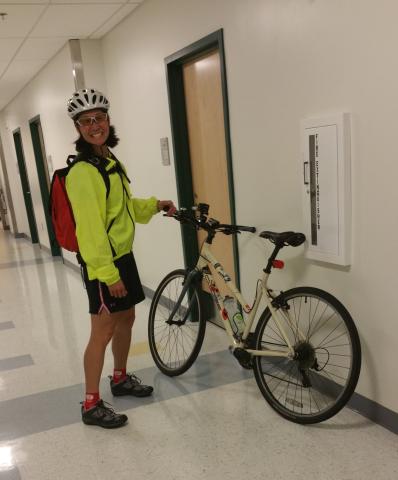 An image of researcher Jessica Chin with her bike. She is wearing a white helmet, red backpack, neon green jacket, black shorts, and black cycling shoes.