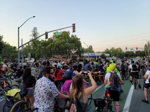 An image of the post pandemic SJBP ride start. A large crowd of people are standing with bicycles under a blue sky.