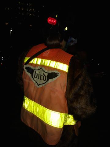 An image of a person wearing an orange vest with yellow reflective tape, with a logo that says "bird" stitched to the back of the vest