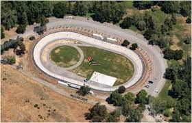 An aerial view of an outdoor velodrome nestled among trees.