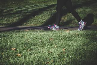 A picture of someone's legs and feet walking through a grass path. The person is wearing black leggings and purple and white running shoes. 