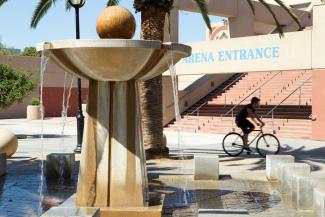 Image of the same fountain as in Image 2 with a person on a bicycle in the background, a palm tree, and a set of stairs.